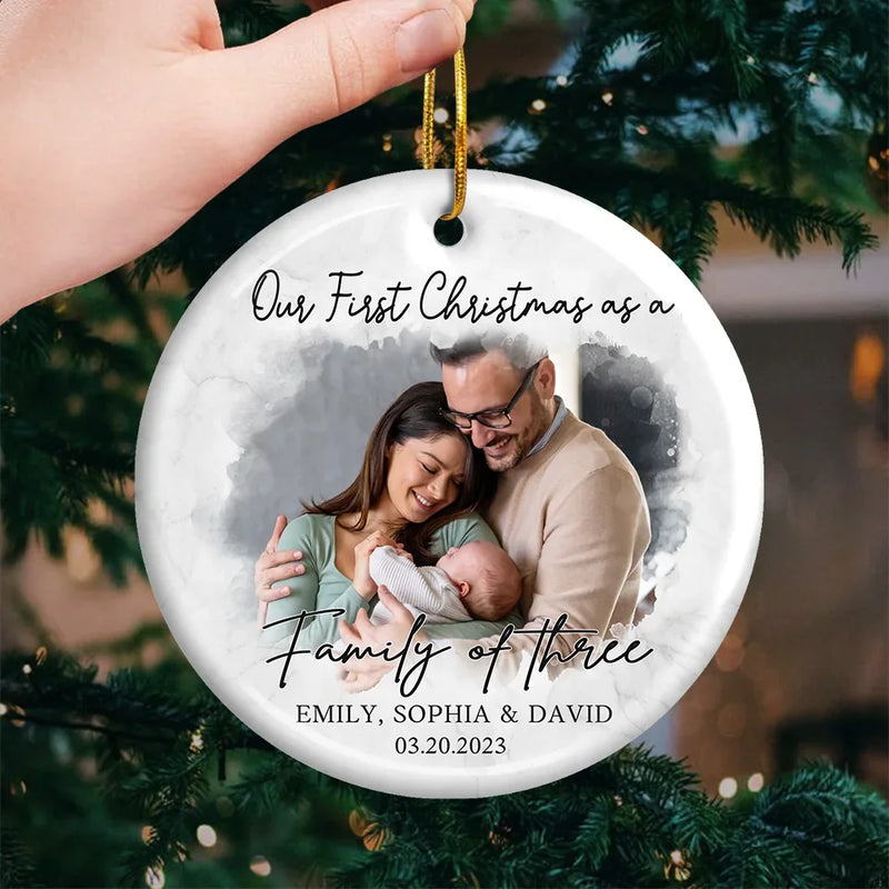Custom Photo Our First Christmas As A Family Of Three - Couple Personalized Custom Ornament - Ceramic Round Shaped - Christmas Gift For Husband Wife, Anniversary, First Christmas